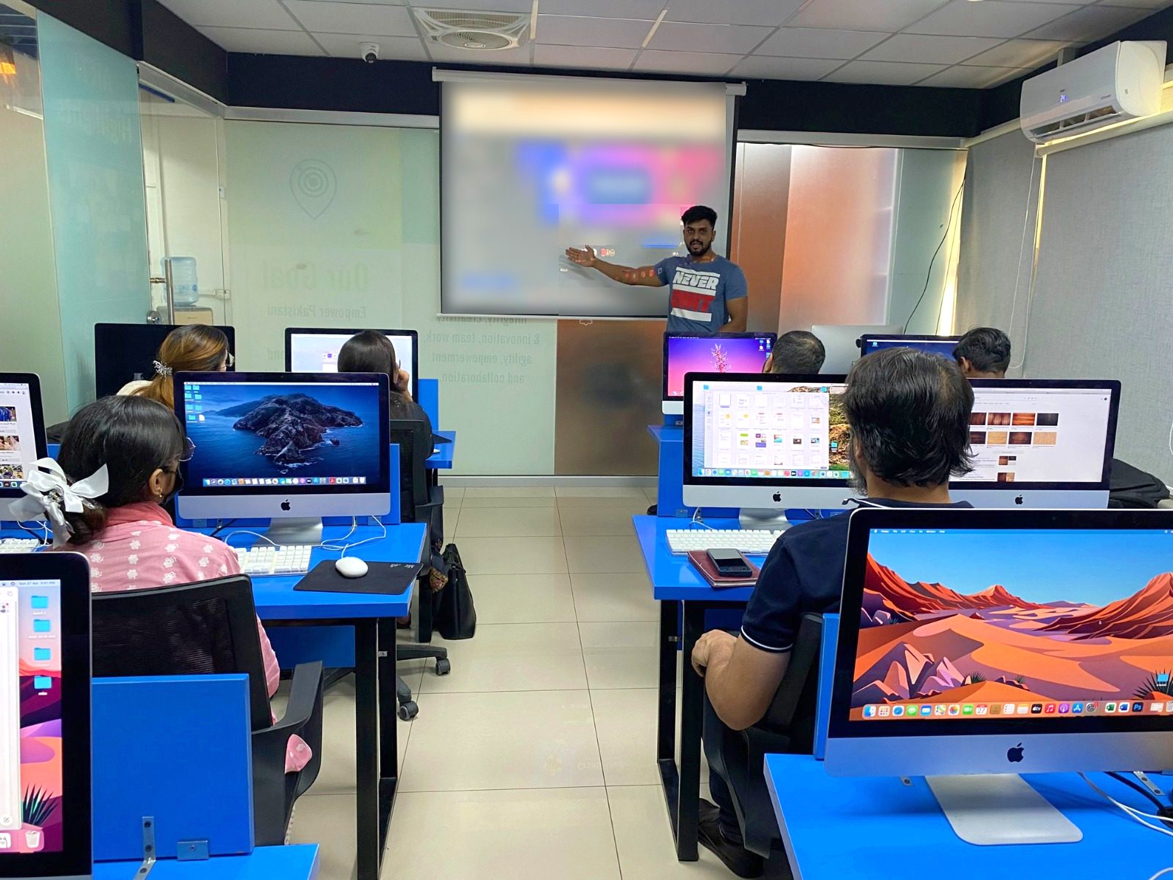 A BBT instructor presenting to students at iMac workstations on the Lahore campus